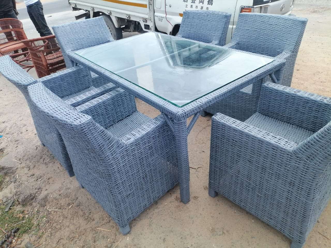 7-piece, poly-rattan outdoor dining set features a rectangular table with a glass top and six matching chairs